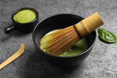 Photo of Cup of fresh green matcha tea with bamboo whisk and spoon on grey table