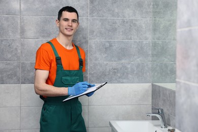Young plumber writing results of examining sink in bathroom