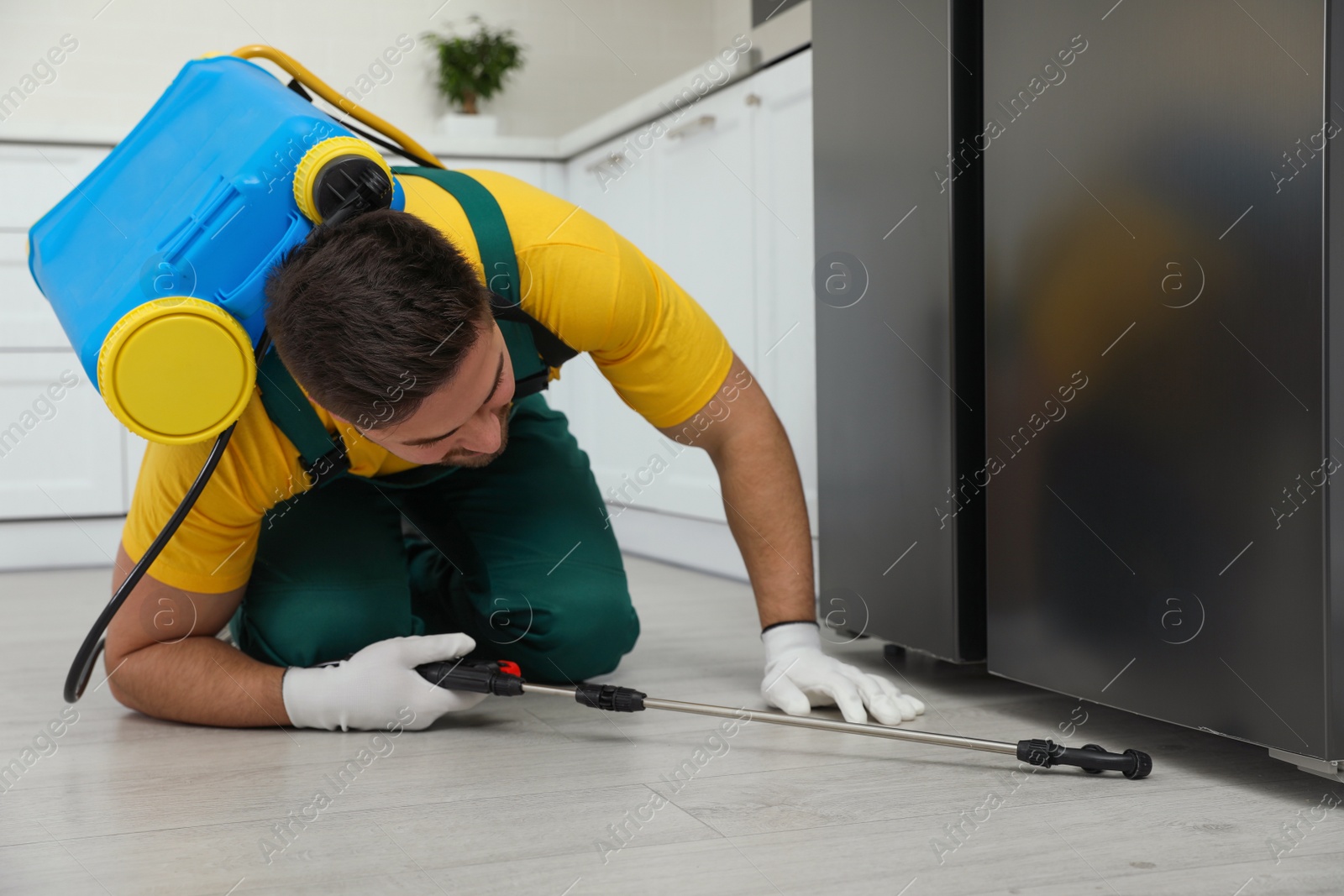 Photo of Pest control worker spraying insecticide under refrigerator in kitchen