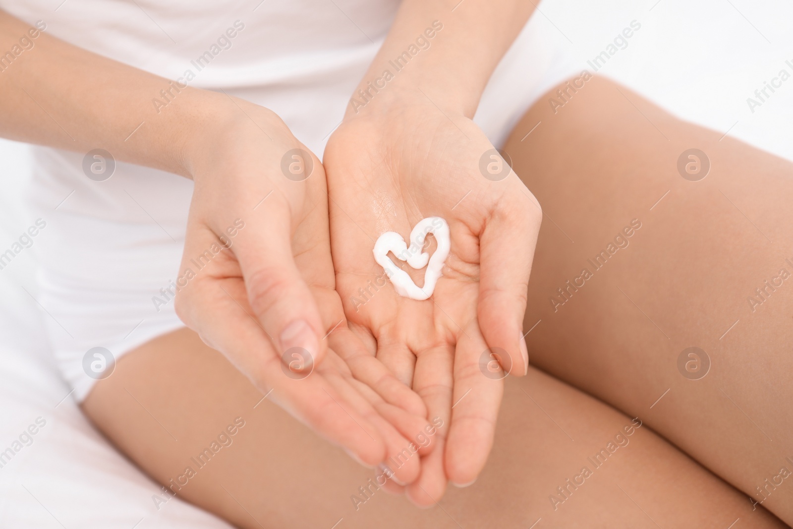 Photo of Young woman with heart made of cream on her hand, closeup. Beauty and body care