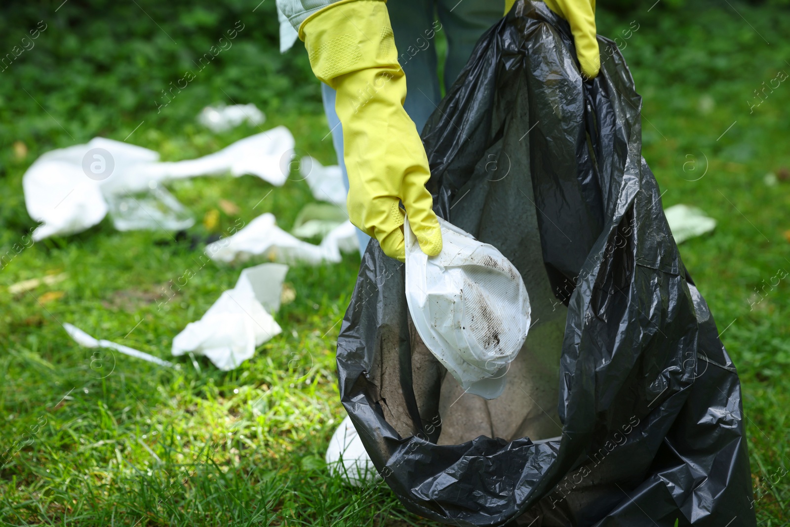 Photo of Woman with plastic bag collecting garbage on green grass outdoors, closeup