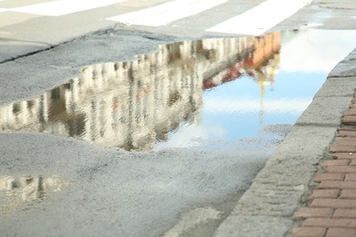 Reflection of buildings in rippled puddle water on asphalt