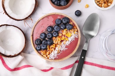 Bowl of delicious fruit smoothie served with fresh blueberries, granola and coconut flakes on white marble table, flat lay