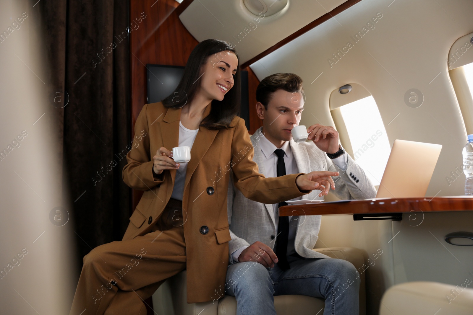 Photo of Colleagues working with laptop at table in airplane during flight