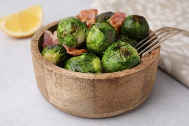 Photo of Delicious roasted Brussels sprouts and bacon in bowl on light table, closeup