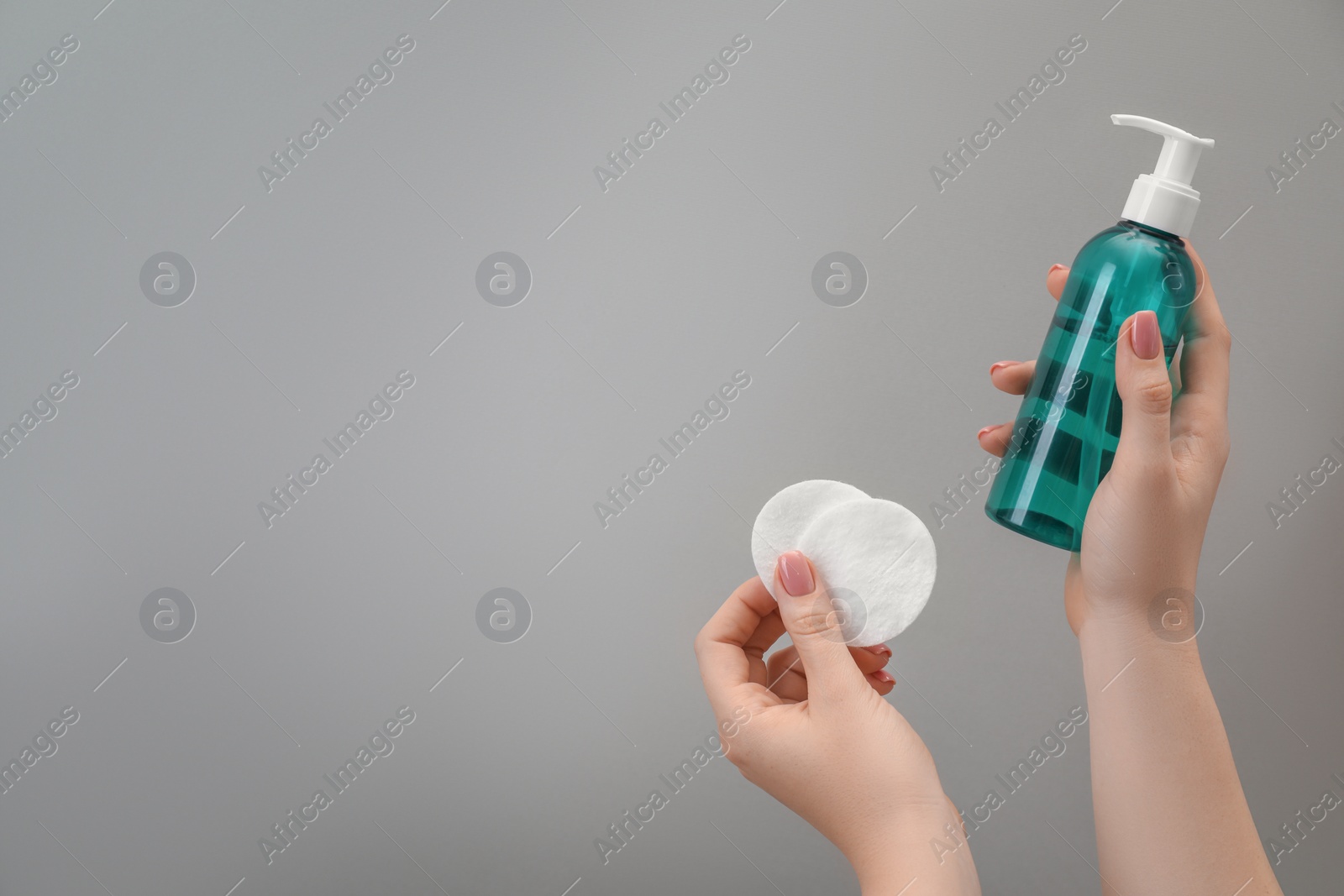 Photo of Woman holding makeup remover and cotton pads on light grey background, closeup. Space for text