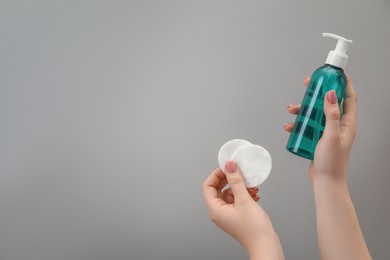 Woman holding makeup remover and cotton pads on light grey background, closeup. Space for text