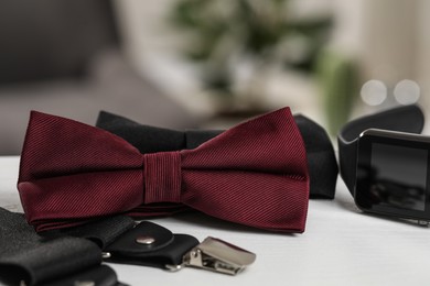 Photo of Stylish color bow ties, suspenders and smartwatch on white wooden table, closeup