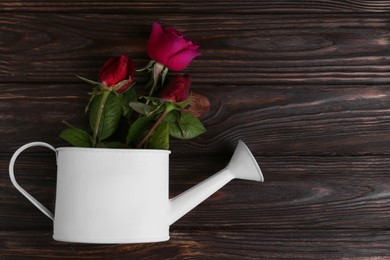 Photo of Beautiful bouquet of pink roses in watering can on wooden table, top view. Space for text