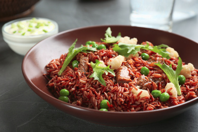 Photo of Tasty brown rice with meat and vegetables on dark grey table, closeup