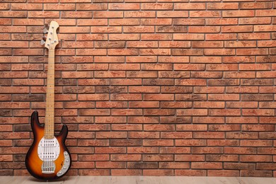 Modern electric guitar near red brick wall indoors. Space for text