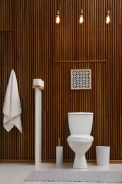 Photo of White toilet bowl near wooden wall in modern bathroom interior