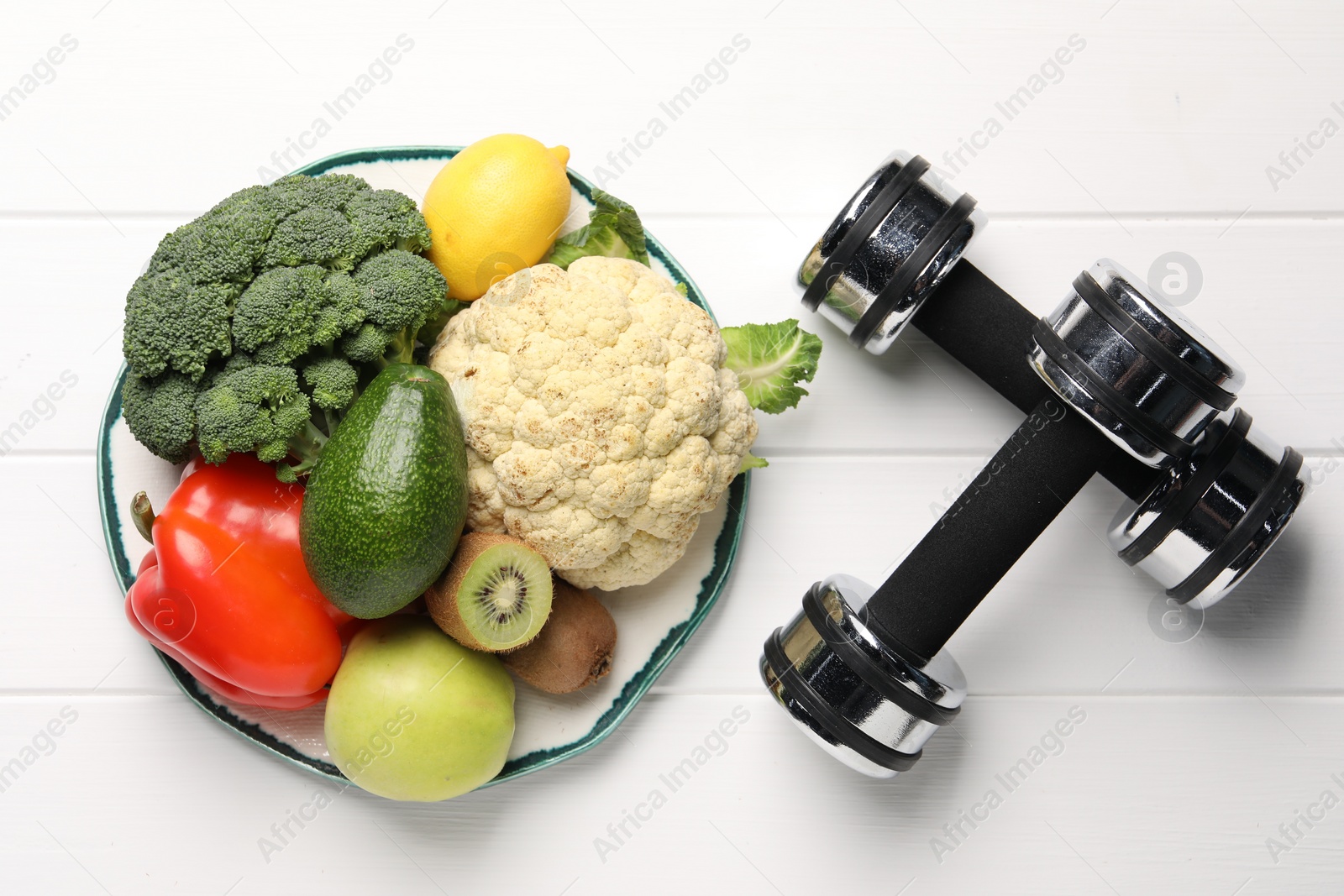 Photo of Healthy diet. Plate with products and dumbbells on white wooden table, flat lay