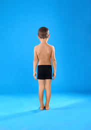 Little boy in underwear on light blue background, back view