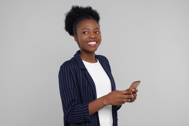 Photo of Happy young woman with smartphone on light grey background
