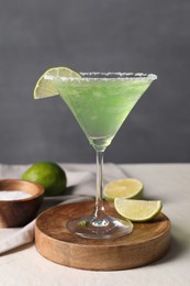 Delicious Margarita cocktail in glass, salt and limes on light table