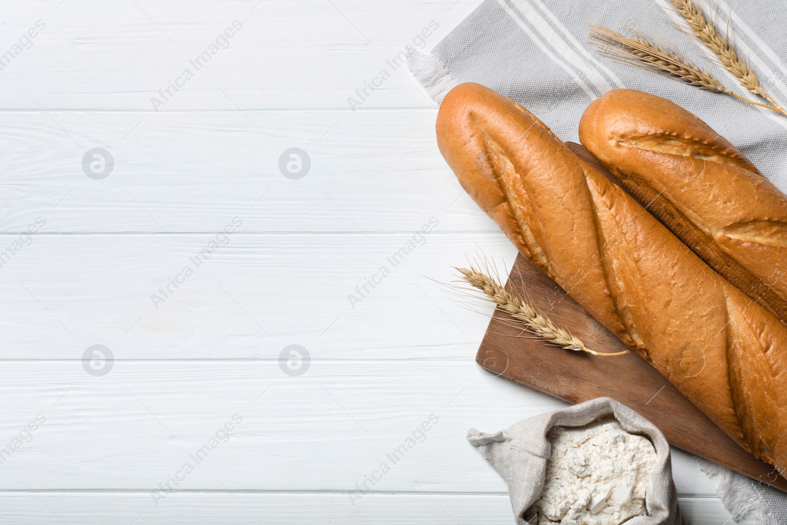 Photo of Fresh tasty baguettes, flour and spikelets on white wooden table, flat lay. Space for text