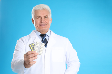 Photo of Senior pharmacist with pills on light blue background