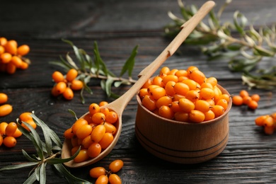 Photo of Ripe sea buckthorn berries on black wooden table, closeup