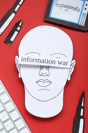 Information warfare concept. Human blinded with propaganda in media field. Flat lay composition paper cutouts and keyboard on red background
