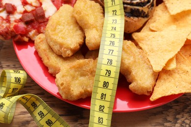 Photo of Different unhealthy food and measuring tape on wooden table, closeup. Weight loss concept