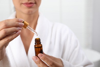 Photo of Woman with bottle of cosmetic serum and dropper on light background, closeup