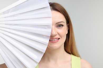 Photo of Happy woman with white hand fan on light grey background