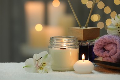 Beautiful composition with different spa products and flowers on white towel against blurred lights, closeup. Space for text