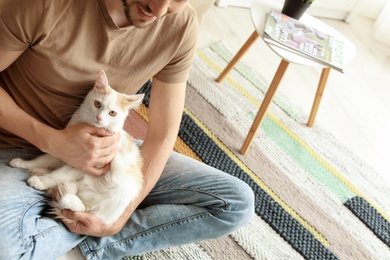 Young man with cute cat sitting on floor at home