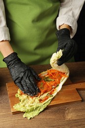 Photo of Woman preparing spicy cabbage kimchi at wooden table against dark background, closeup