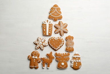 Christmas tree shape made of delicious decorated gingerbread cookies on white wooden table, flat lay