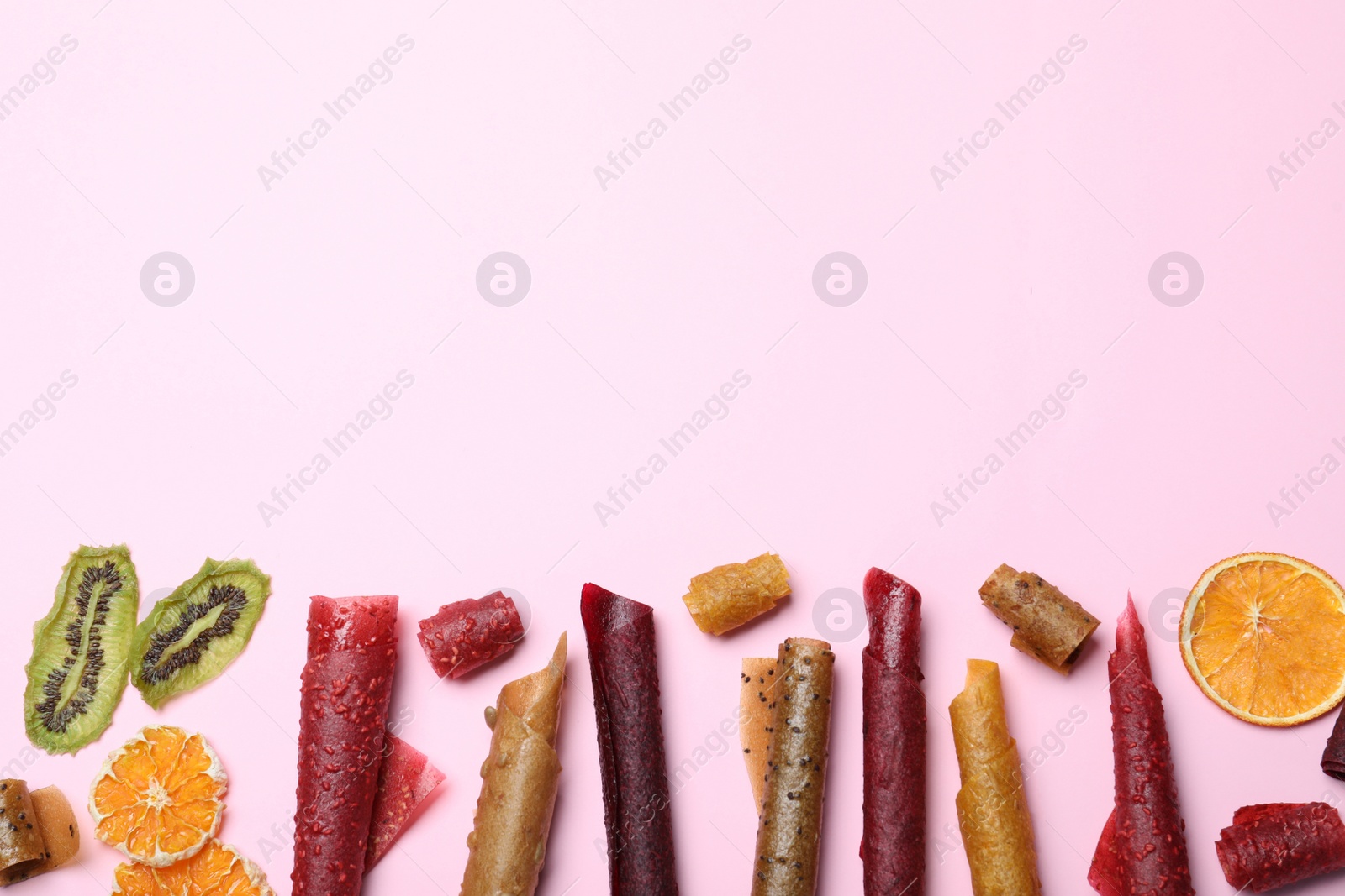 Photo of Delicious fruit leather rolls on pink background, flat lay. Space for text