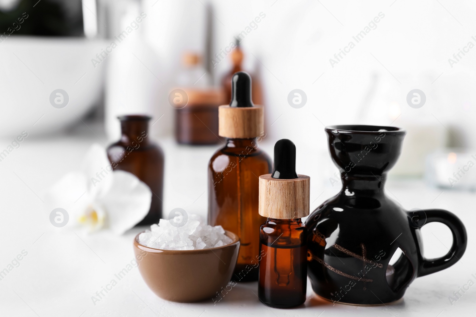 Photo of Essential oils, sea salt and aroma lamp on white table in bathroom, closeup. Space for text