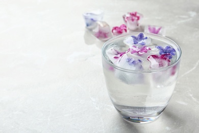 Glass of water with floral ice cubes on table. Space for text