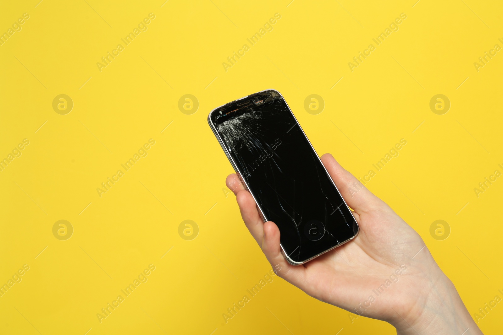 Photo of Woman holding damaged smartphone on yellow background, closeup with space for text. Device repairing