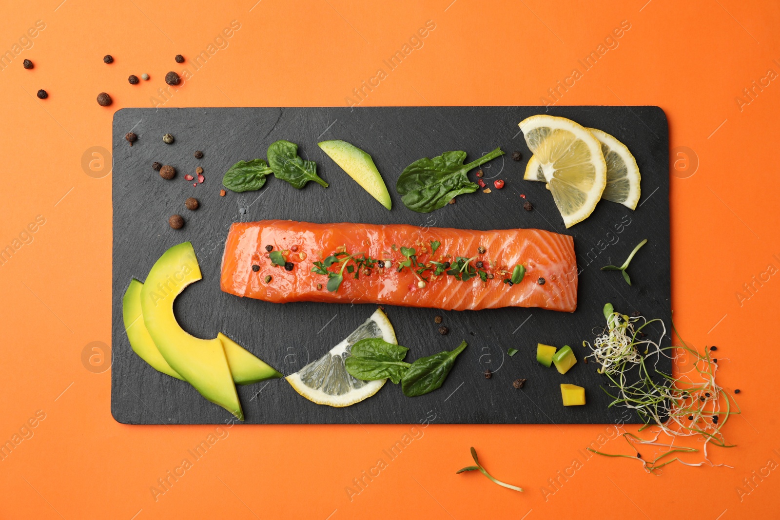 Photo of Delicious salmon with spinach, lemon and avocado on orange background, flat lay