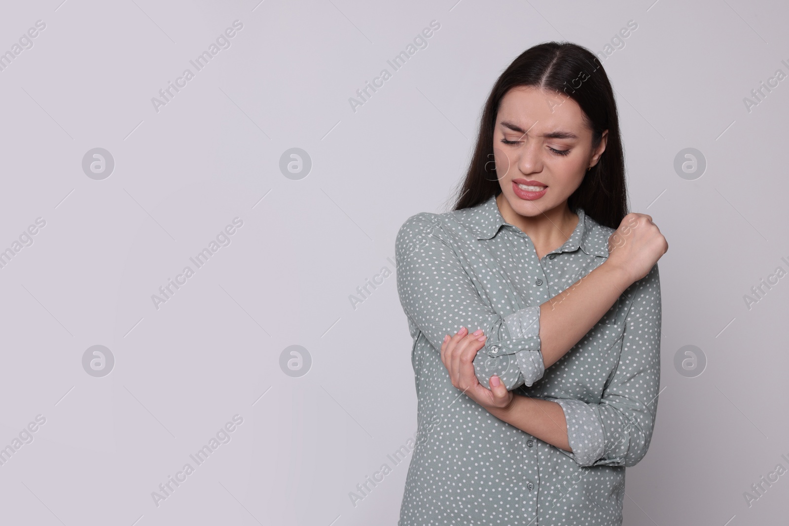 Photo of Young woman suffering from pain in elbow on light grey background, space for text. Arthritis symptoms