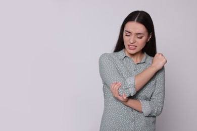 Photo of Young woman suffering from pain in elbow on light grey background, space for text. Arthritis symptoms