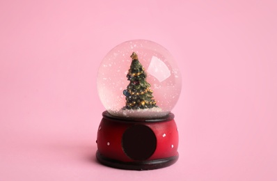 Photo of Beautiful snow globe with Christmas tree on pink background