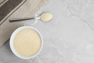 Gelatin powder in bowl and spoon on light grey marble table, flat lay. Space for text