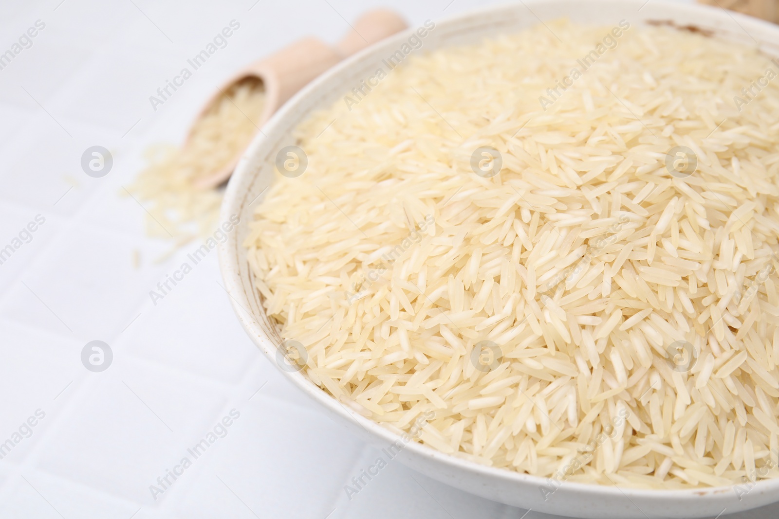Photo of Raw rice in bowl on white tiled table, closeup. Space for text