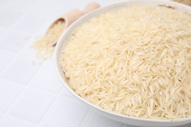 Raw rice in bowl on white tiled table, closeup. Space for text