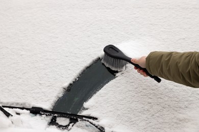 Woman cleaning car windshield from snow with brush, closeup