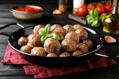 Photo of Tasty cooked meatballs with basil on black wooden table