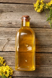 Photo of Rapeseed oil in glass bottle and beautiful yellow flowers on wooden table, flat lay