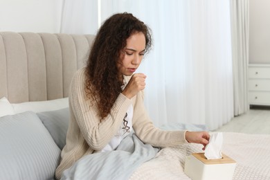 Sick African American woman with box of tissues in bed at home