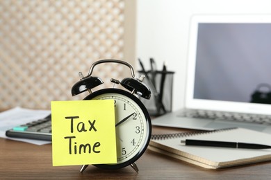 Alarm clock and reminder note with words Tax Time on wooden table. Space for text