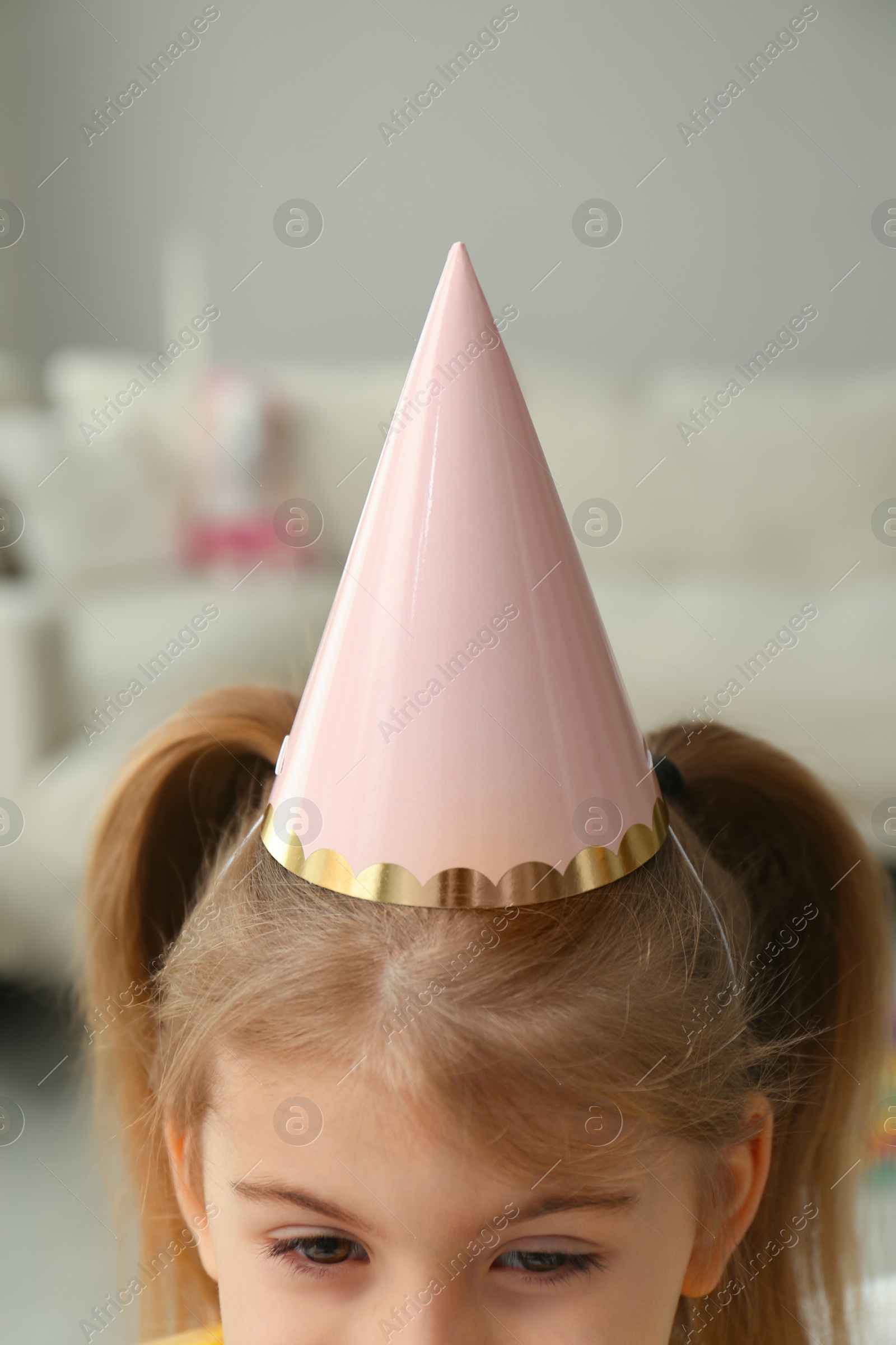 Photo of Cute little girl wearing party hat at home