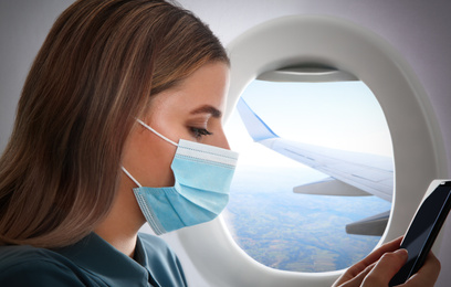 Image of Traveling by airplane during coronavirus pandemic. Woman with face mask and phone near porthole