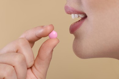 Woman taking pill on beige background, closeup